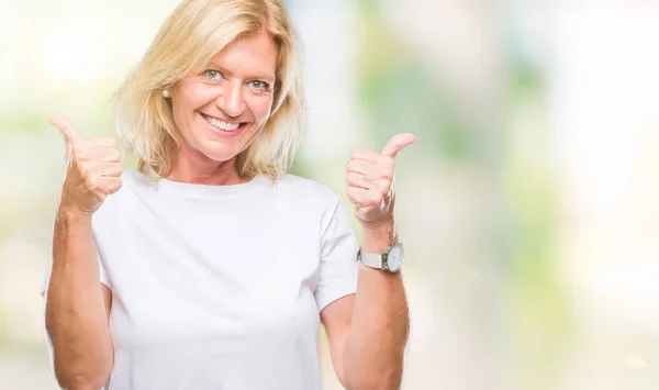 Middle age blonde woman over isolated background success sign doing positive gesture with hand, thumbs up smiling and happy. Looking at the camera with cheerful expression, winner gesture.