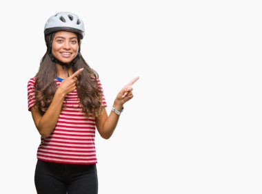 Gülümseyen ve iki elleri ve parmakları ile tarafına işaret kamera bakarak izole arka plan üzerinde güvenlik kask giyen genç Arap bisikletçi kadın.