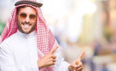 Keffiyeh gülümseyen ve iki elleri ve parmakları ile tarafına işaret kamera bakarak izole arka plan üzerinde giyen genç yakışıklı adam.