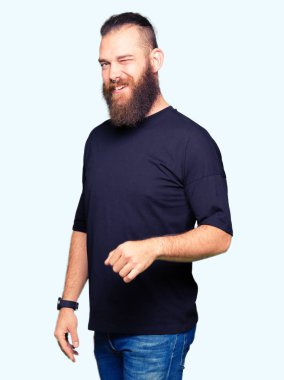 Genç sarışın adam giyiyor rahat t-shirt seksi bir ifadeyle, neşeli ve mutlu yüzünü kameraya bakarak göz kırpıyor.