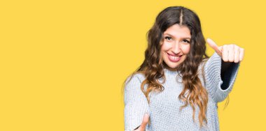 Kış kazak onaylama giyen genç güzel kadın el ile pozitif jest yapıyor gülümseyen ve başarı için mutlu yaşasın. Kamera, kazanan jest arıyorsunuz.