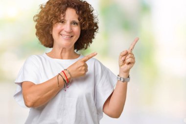 Gülümseyen ve iki elleri ve parmakları ile tarafına işaret kamera bakarak izole arka plan üzerinde beyaz t-shirt giyen kadın güzel orta ager kıdemli.