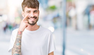Beyaz t-shirt üzerinde izole giyen genç yakışıklı adam arka plan işaret jest göz izlemek için şüpheli ifade