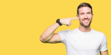 Neşeli gülümseyen casual beyaz t-shirt işaretçi el parmak yüz ve burun, giyen yakışıklı adam