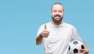 Futbol futbol topu tutan genç beyaz hipster adam arka plan mutlu ok işareti, başparmak ile parmak, mükemmel işareti yapıyor kocaman bir gülümseme ile izole