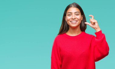 İzole arka plan gülümseyen ve boyutu işaret parmaklı ararken ve kamera işi el ile kendinden emin eller üzerinde kış kazak giyen genç güzel Arap kadın. Ölçü kavramı.