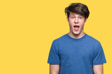 Korkuyor ve şok sürpriz ifade, korku ve heyecan yüz ile izole arka plan üzerinde mavi t-shirt giyen genç yakışıklı adam.
