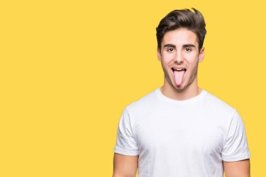 Genç yakışıklı dilini izole arka plan üzerinde beyaz t-shirt giyen adam out komik ifade ile mutlu. Duygu kavramı.