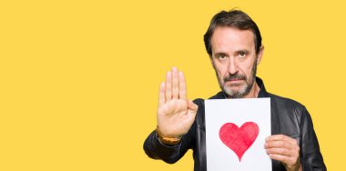 Açık eliyle dur işareti ile ciddi ve kendine güvenen ifade, savunma jest yapıyor kırmızı kalp ile kağıt tutan yakışıklı orta yaş erkek