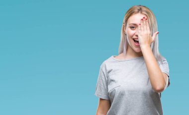 Sarışın genç kadın el yüz ve sürpriz duygu kendinden emin gülümseme ile tek gözüyle kapsayan izole arka plan üzerinde.