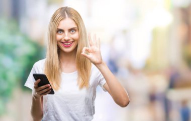 Genç güzel sarışın kadın parmakları, mükemmel sembolü olan ok işareti yapıyor izole arka plan üzerinde akıllı telefon kullanma