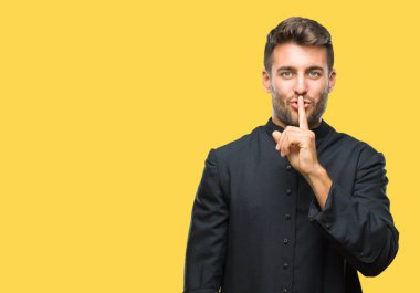 Young catholic christian priest man over isolated background asking to be quiet with finger on lips. Silence and secret concept. clipart