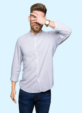 Şoka girmiş genç yakışıklı bir adam elleriyle yüzünü ve gözlerini kapatıyor, utanmış bir ifadeyle parmaklarından bakıyor..