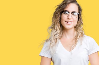 Arka plan eller üzerinde gözlük güzel sarışın genç kadın birlikte izole ve rahat ve neşeli gülümseyen parmak çarpı işareti. Başarı ve iyimser