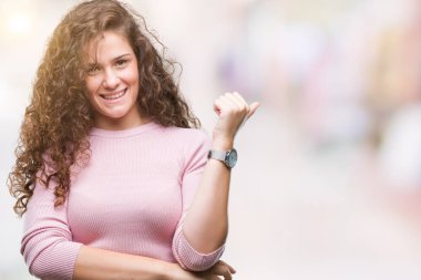 Seyir ve başparmak yanında yukarıyı mutlu yüz ile gülümseyen izole arka plan üzerinde pembe kazak giyen güzel esmer kıvırcık saçlı Genç kız.