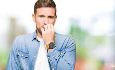 Stresli ve gergin elle çivi ısırma ağzına seyir kot ceket giyen sakal ve mavi gözlü yakışıklı adam. Anksiyete sorunu.