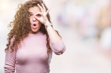 Güzel esmer kıvırcık saçlı Genç kız ok jest sürpriz yüz, göz parmaklarının arasından seyir şok yapıyor izole arka plan üzerinde pembe kazak giyiyor. İmansız ifade.