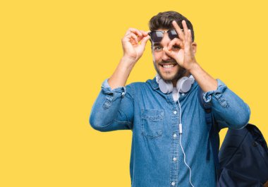 Gülümseyerek el parmakları ile mutlu yüz üzerinden seyir göz ile ok jest yapıyor izole arka plan üzerinde kulaklık ve sırt çantası giyen genç yakışıklı turist adam.