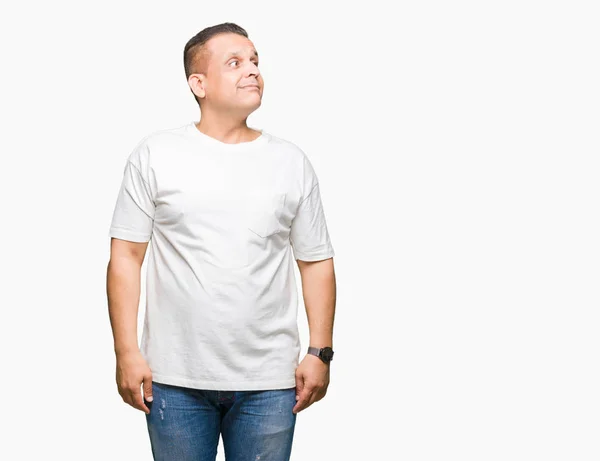 中年阿拉伯男子穿白色 T恤在孤立的背景微笑看一边 盯着思考 — 图库照片