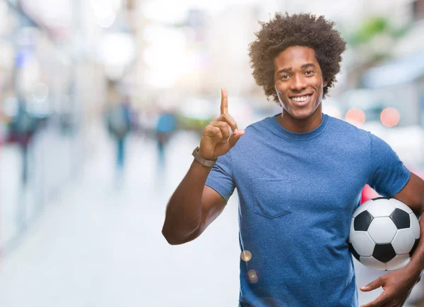 アフロ アメリカ人持株サッカー ボールのアイデアに驚いて孤立の背景の上や幸せそうな顔 ナンバーワンと人差し指の質問 — ストック写真