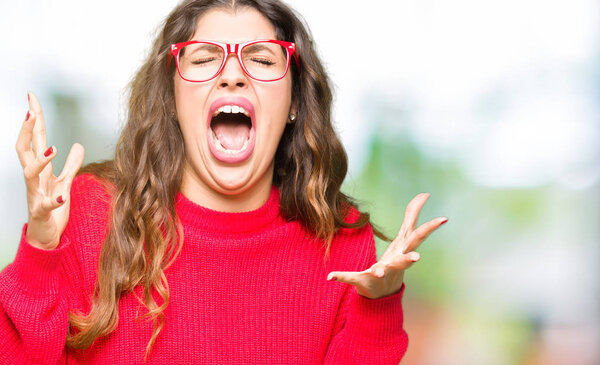 Young beautiful woman wearing red glasses crazy and mad shouting and yelling with aggressive expression and arms raised. Frustration concept.