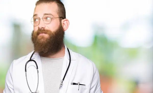 Joven Doctor Rubio Con Barba Vistiendo Abrigo Médico Sonriendo Mirando — Foto de Stock