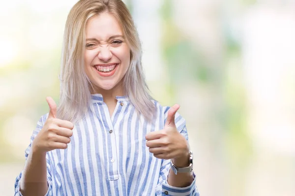 Young blonde woman over isolated background approving doing positive gesture with hand, thumbs up smiling and happy for success. Looking at the camera, winner gesture.