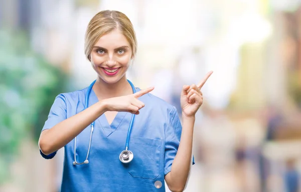 Young beautiful blonde doctor surgeon nurse woman over isolated background smiling and looking at the camera pointing with two hands and fingers to the side.