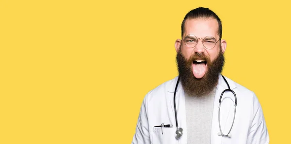 年轻的金发医生与胡子穿着医疗外套伸出舌头出来高兴与搞笑的表情 情感概念 — 图库照片