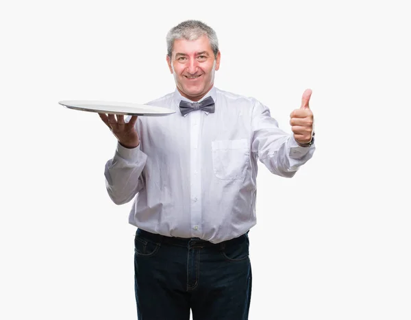 英俊的高级服务员拿着银盘在孤立的背景高兴与灿烂的微笑做确定的标志 用手指竖起大拇指 优秀的标志 — 图库照片