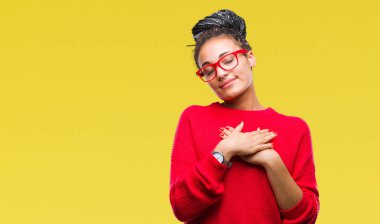 Genç örgülü saç Afro-Amerikan Kız göğüs kapalı gözlerle ellerinde ve yüzünde minnettar jest ile gülümseyen izole arka plan üzerinde kazak ve gözlük takıyor. Sağlık kavramı.