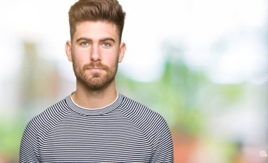 Yüzünde çizgili süveter gevşek ciddi ifade ile giyen genç yakışıklı adam. Basit ve doğal kameraya bakıyor.