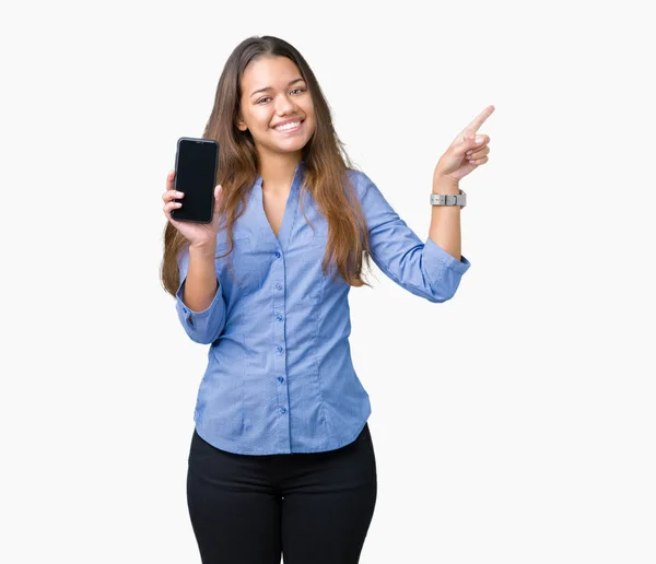 年轻美丽的黑发女商人在孤立的背景显示智能手机屏幕非常高兴用手和手指指向一边 — 图库照片