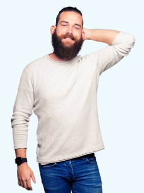 Genç sarışın çekici poz giyen sıradan kazak gülen emin dokunaklı saç el jest, yukarı ile adam