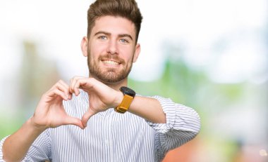 Kalp simgesi ve elleriyle şekil gösterilen aşık gülümseyen yakışıklı delikanlı. Romantik kavramı.