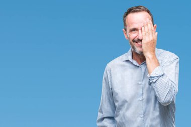 Orta yaş ağarmış üst düzey iş adamı el yüz ve sürpriz duygu kendinden emin gülümseme ile tek gözüyle kapsayan izole arka plan üzerinde.