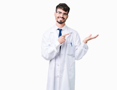 Hayret ve el ile sunulması ve parmak ile işaret ederken kameraya gülümseyen izole arka plan üzerinde beyaz önlük giyen genç profesyonel bilim adamı.