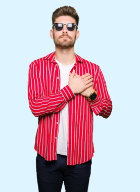 Yakışıklı delikanlı ile gülümseyen güneş gözlüğü takıyor kapalı gözler ve yüzünde minnettar jest ile göğüs üzerinde eller. Sağlık kavramı.