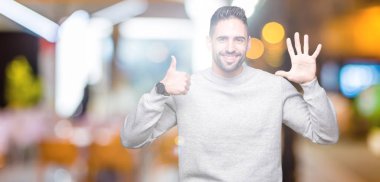 Gösterilen arka plan üzerinde sweatshirt giyen genç yakışıklı adam izole ve parmakları ile işaret kendinden emin ve mutlu gülümseyerek süre 6 numara.