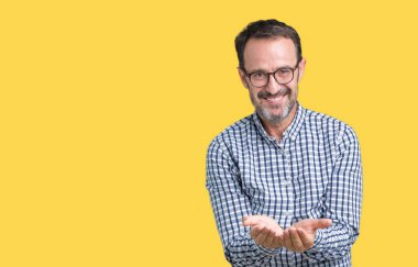 Yakışıklı orta yaş zarif kıdemli adam gözlük izole üzerinde arka plan gülen alma veya jest vererek birlikte el avuç içi ile. Ayrı tutma ve koruma