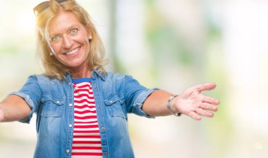 Orta yaş sarışın kadın sarılmak için kollarını açarak gülümseyerek kameraya bakarak izole arka plan yüzünden. Neşeli ifade kucaklayan mutluluk.