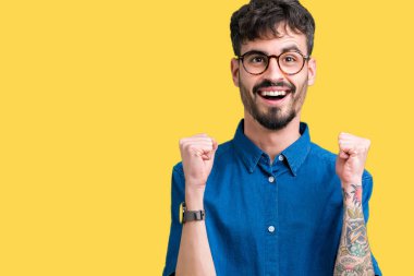 Yakışıklı delikanlı izole arka plan üzerinde kutluyor gözlük takan şaşırttı ve başarı için kaldırdı kollarını açarak hayret ve gözleri açık. Kazanan kavramı.