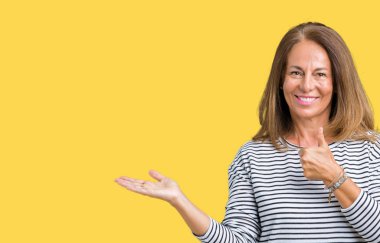 Giyen güzel orta yaş kadın kazak izole arka plan gösteren palm el ve iş tamam jestle üzerinde başparmak yukarı, gülümseyen mutlu ve neşeli çizgili.