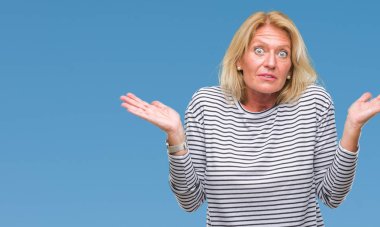 Orta yaş sarışın kadın izole arka plan clueless ve şaşkın bir ifadeyle kollar ve eller kaldırdı. Şüphe kavramı.