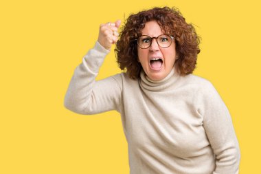 Boğazlı kazak ve gözlük kızgın ve kızgın izole arka plan üzerinde giyen güzel orta ager üst düzey kadın hayal kırıklığı ve öfke ile bağırarak süre öfkeli yumruk yükselterek. Öfke ve agresif kavramı.