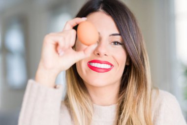 Ayakta ve diş gösterilen kendine güvenen bir gülümsemeyle gülümseyerek mutlu bir yüz ile taze yumurta evde tutan genç güzel kadın