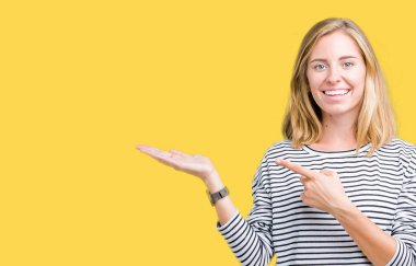 Hayret ve el ile sunulması ve parmak ile işaret ederken kameraya gülümseyen izole arka plan üzerinde çizgili süveter giyen güzel genç kadın.