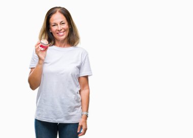 Orta yaş İspanyol kadın kek yeme izole arka plan üzerinde duran ve diş gösterilen kendine güvenen bir gülümsemeyle gülümseyerek mutlu bir yüz ile