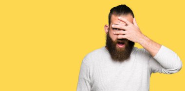 Mahcup ifadeyle parmaklarımın arasından seyir yüz ve gözler el ile kapsayan şok rahat kazak bakmak giyen genç sarışın adam.