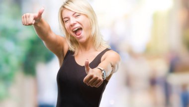 Genç güzel sarışın çekici kadın el ile pozitif jest yapıyor onaylama izole arka plan üzerinde zarif elbise başparmak gülümseyen ve başarı için mutlu. Kamera, kazanan jest arıyorsunuz.